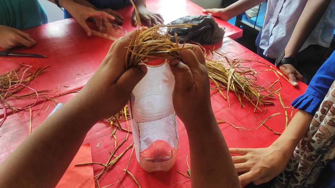 A student's hands adding straw to a plastic bottle to turn it into a bird feeder