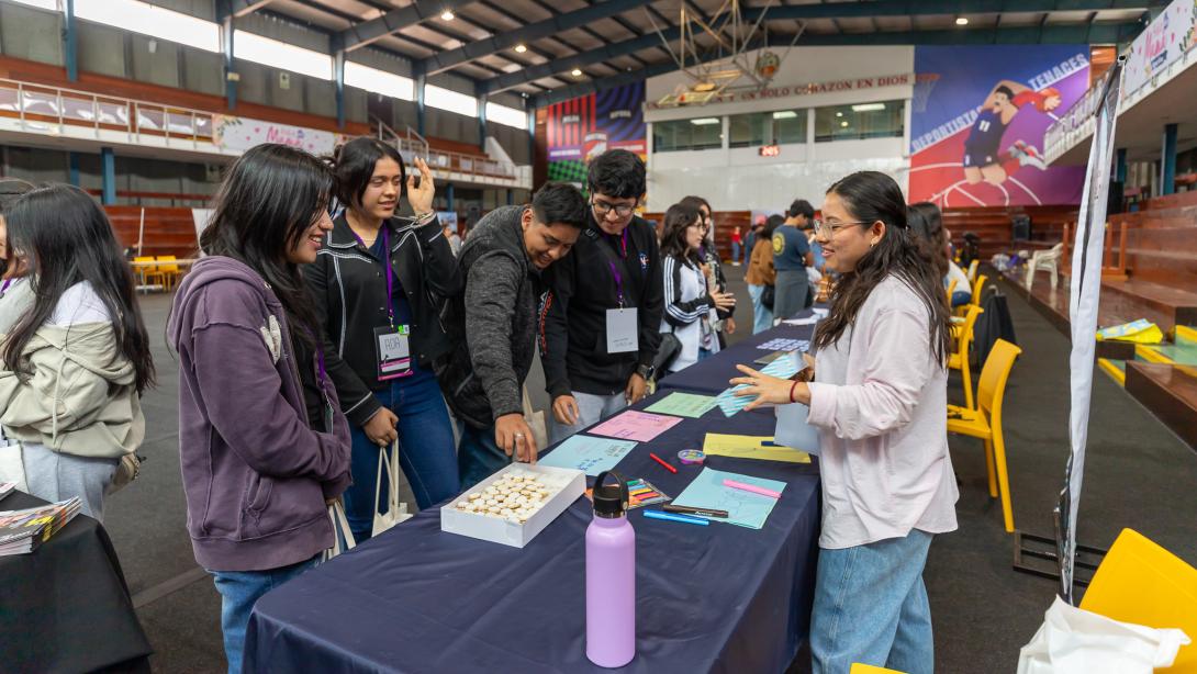 A group of four students stand in front of a desk at a fair talking to the presenter