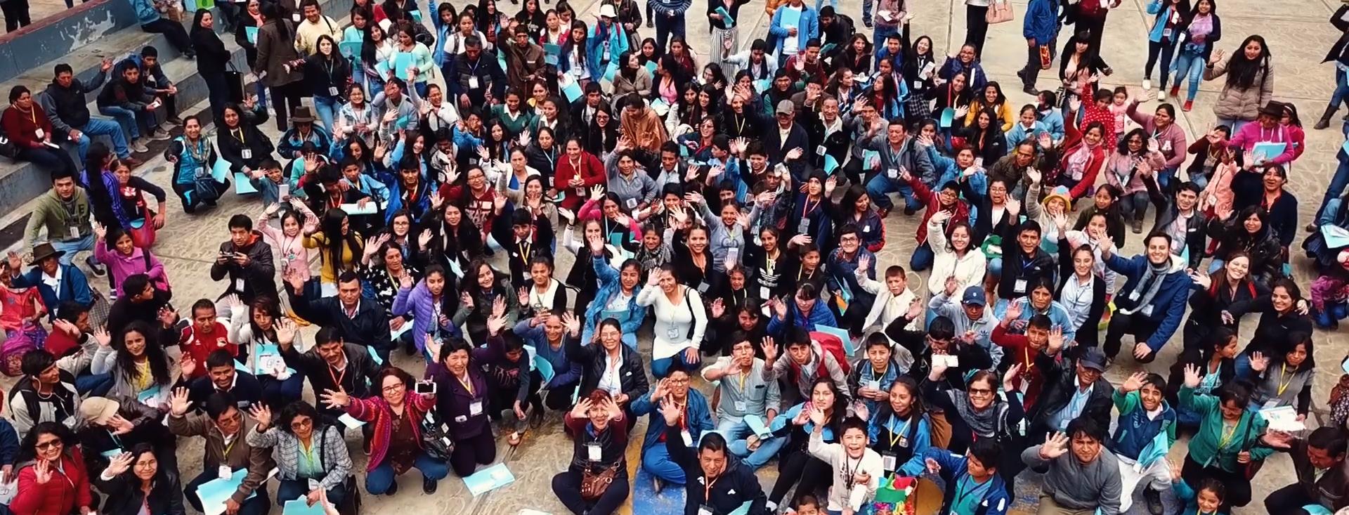 Shot from above, a large crowd of people in an outdoor courtyard look up at the camera