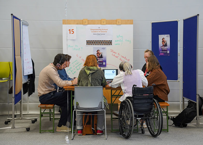 A group of people sit around a table, including a woman in a wheel chair