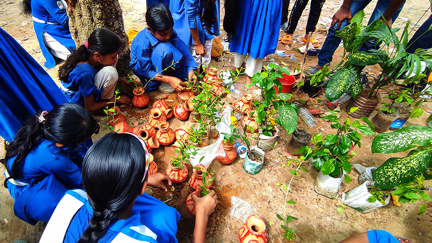 Girls in school uniform gather around plant and tree seedlings in small pots