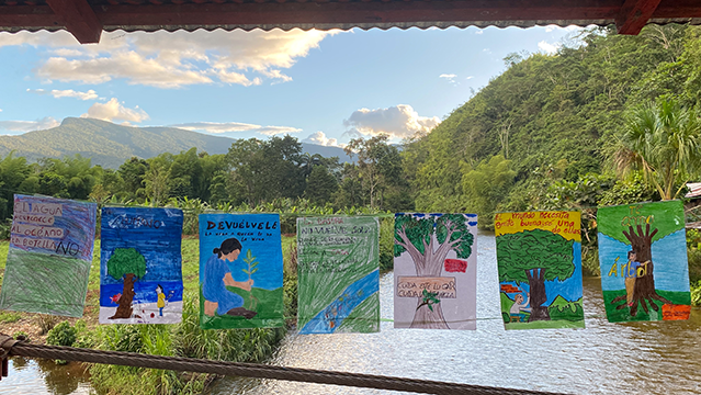 Paintings done by children hang on a string over a lush river valley