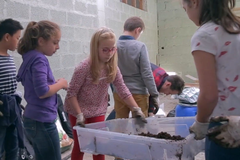Three young girls lift a plastic bin filled with what looks like soil